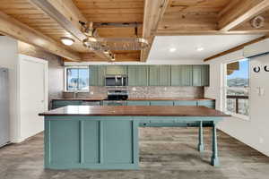 Kitchen featuring green cabinetry, wooden counters, stainless steel appliances, a wood ceiling with exposed beams, and light wood-type flooring