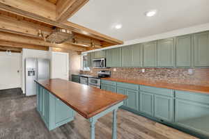 Kitchen with green cabinets, butcher block counters, stainless steel appliances, and dark wood-style floors