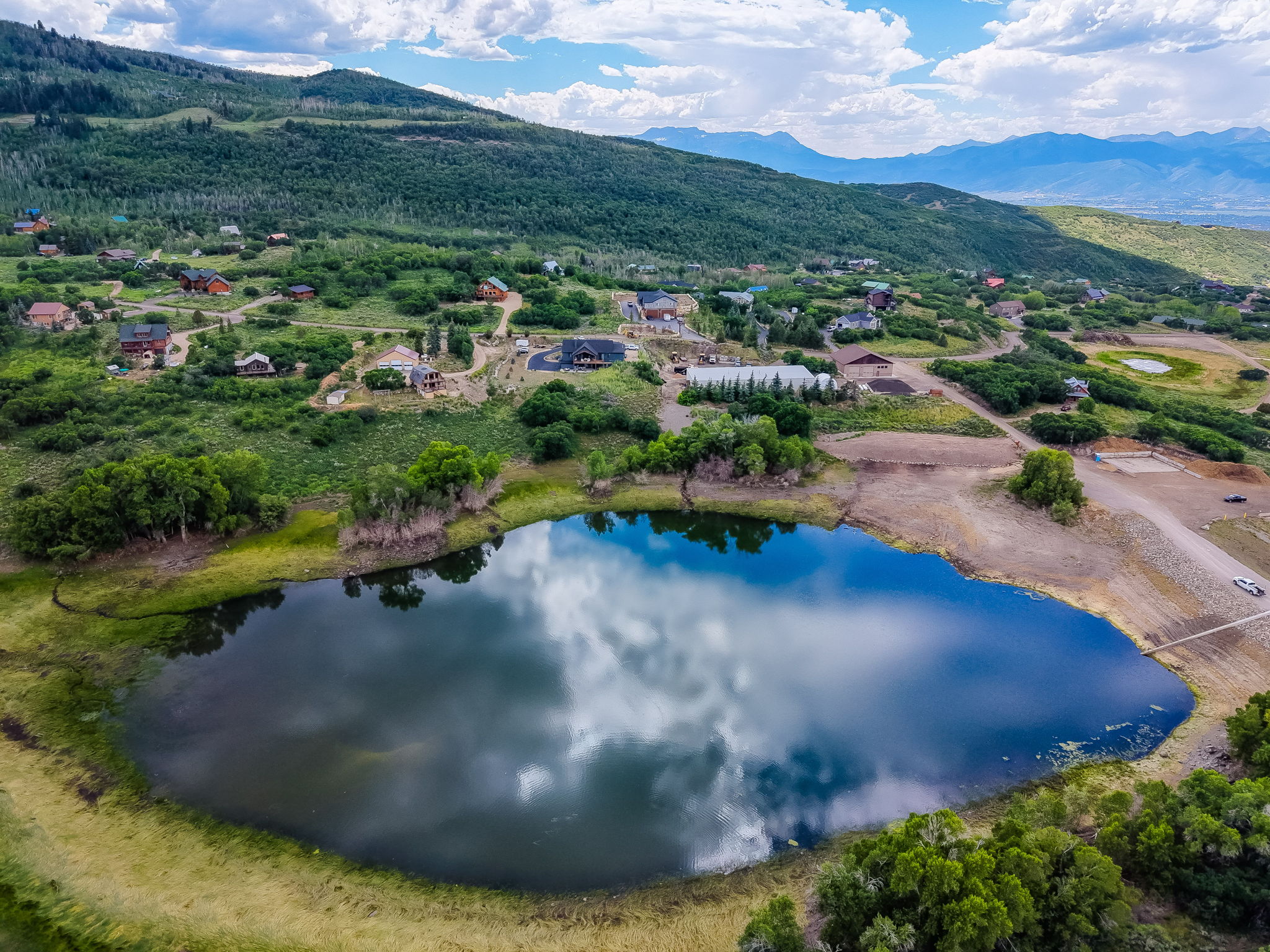 Mountainous landscape featuring a prominent body of water, surrounded by green foliage and distant residential properties