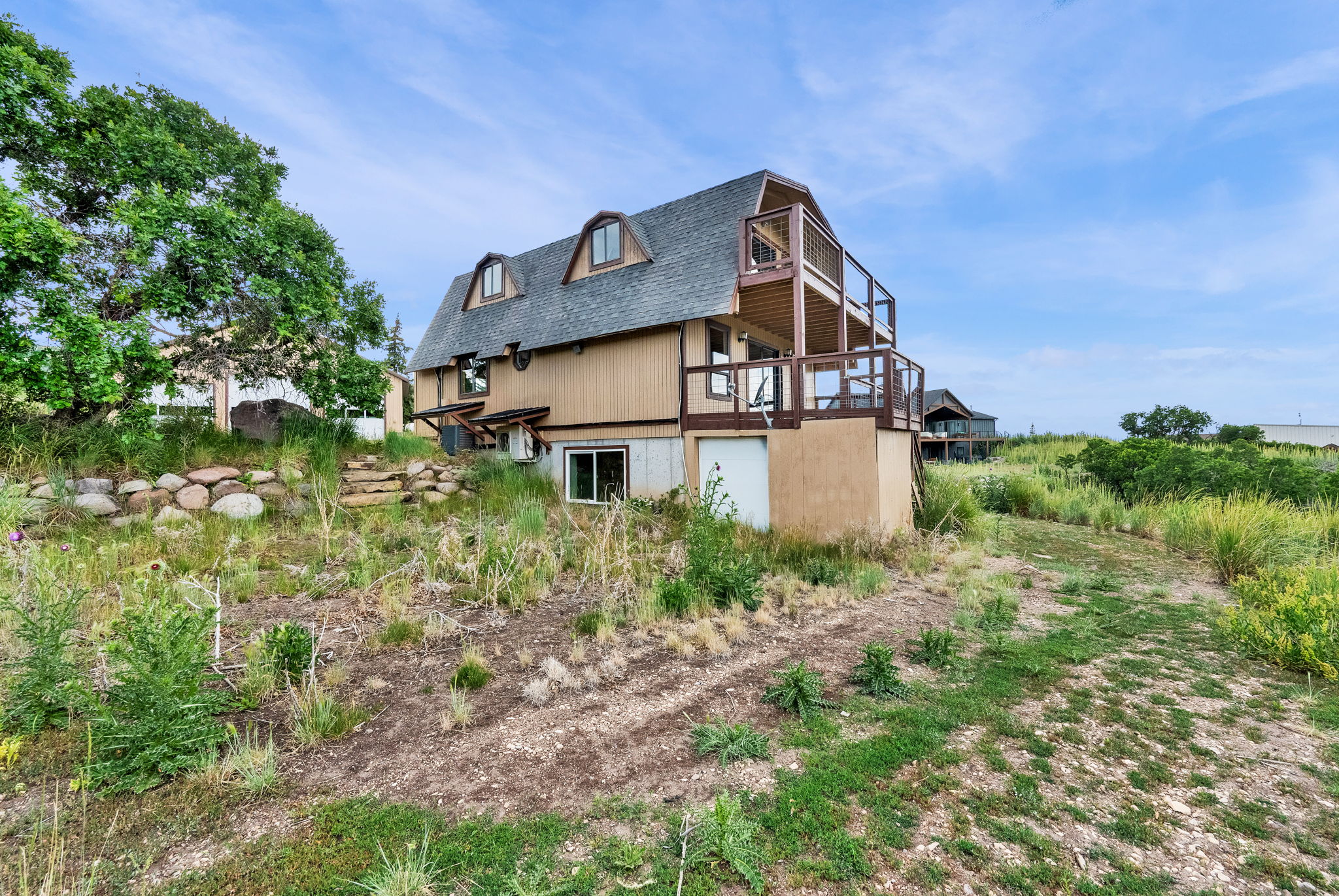 Two-story property featuring a multi-level deck and dormer windows, set on a natural landscape with established trees