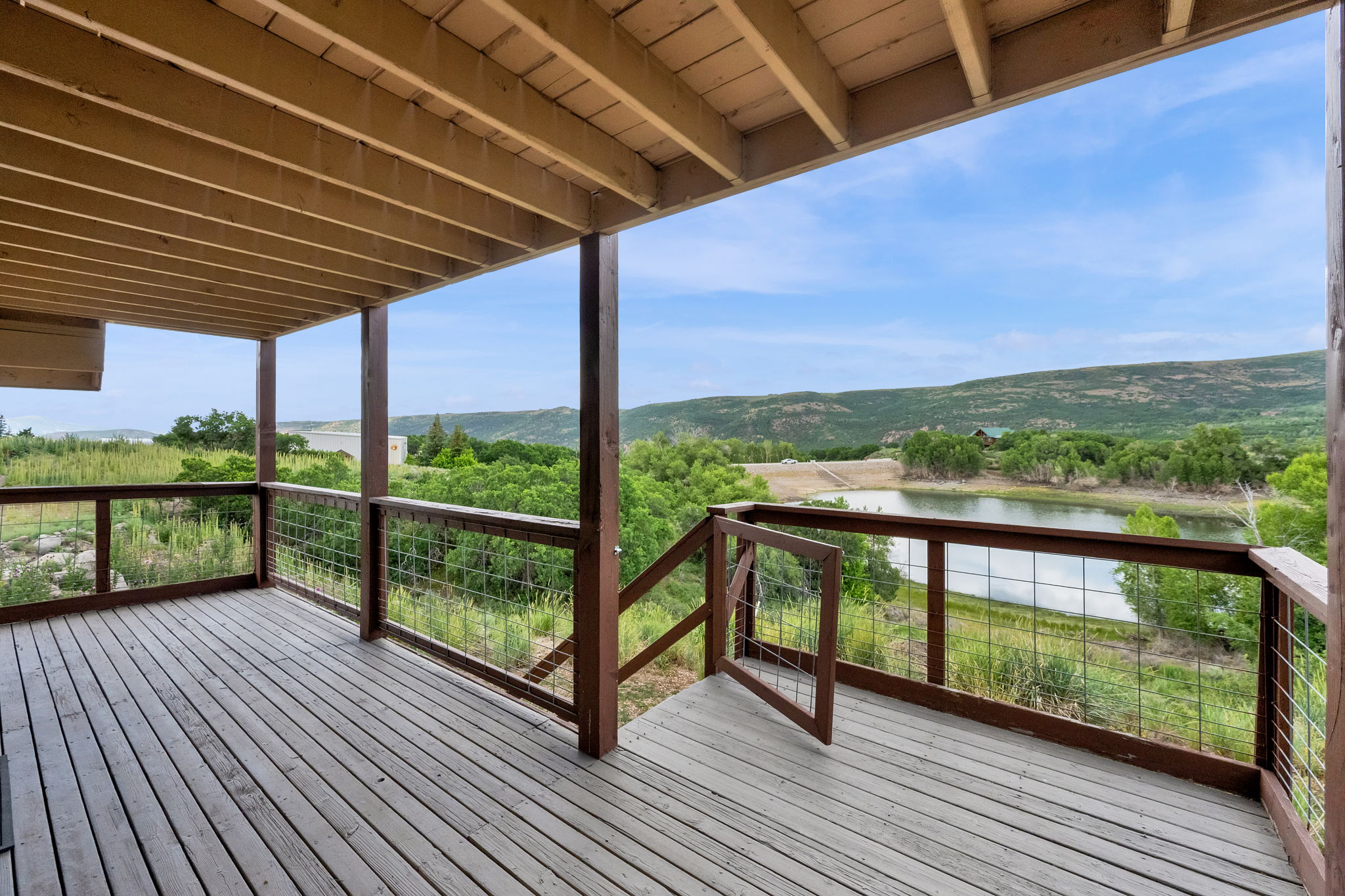 Spacious outdoor deck featuring wood-finish decking, wire-mesh railing, and an expansive mountain and lake backdrop