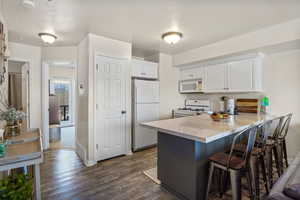 Kitchen featuring a peninsula, white appliances, dark wood finished floors, white cabinetry, and a breakfast bar
