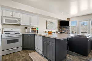 Dual tone kitchen with a kitchen bar, dual tone cabinets, white appliances, open floor plan, and a peninsula