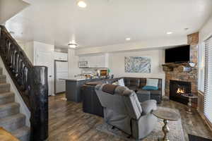 Living room with dark wood-style flooring, a stone fireplace, and recessed lighting