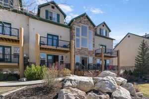 Back of house with stone siding and a balcony