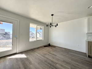 Unfurnished dining area with a textured ceiling, dark wood-style flooring, and a chandelier