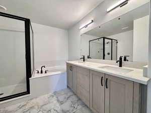 Bathroom featuring a shower stall, double vanity, a garden tub, and a textured ceiling