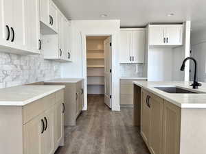 Kitchen featuring dark wood finished floors, recessed lighting, dual tone cabinets, light stone counters, and a kitchen island with sink