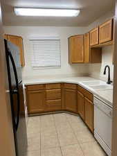 Kitchen featuring light countertops, wood finish cabinets, white dishwasher, freestanding refrigerator, and light tile patterned floors