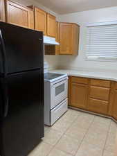 Kitchen featuring freestanding refrigerator, white electric stove, light countertops, and wood finish cabinets