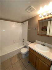 Bathroom with a textured ceiling, vanity, shower / bathtub combination, and light tile patterned floors