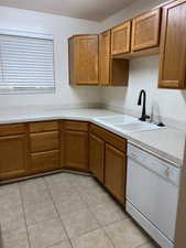Kitchen featuring white dishwasher, wood finish cabinets, light countertops, and light tile patterned flooring