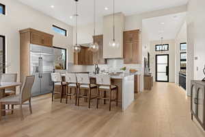 Kitchen with a center island with sink, a breakfast bar, stainless steel built in refrigerator, wood finish cabinetry, and a high ceiling