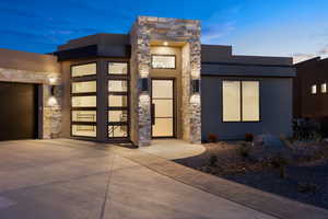 View of front of house with stone siding, stucco siding, a garage, and driveway