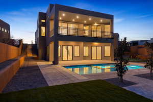 Back of property at dusk with a patio, stucco siding, a fenced backyard, a pool with connected hot tub, and a balcony