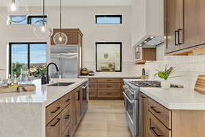 Kitchen with light stone counters, premium appliances, wood finish cabinets, and an island with sink