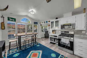 Kitchen with stainless steel appliances, white cabinets, glass insert cabinets, tasteful backsplash, and light wood-type flooring
