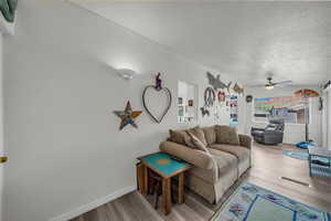 Living room featuring light wood-style floors, a ceiling fan, and a textured ceiling