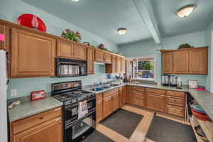 Kitchen featuring black appliances, wood finish cabinetry, a textured ceiling, light wood-style flooring, and beam ceiling