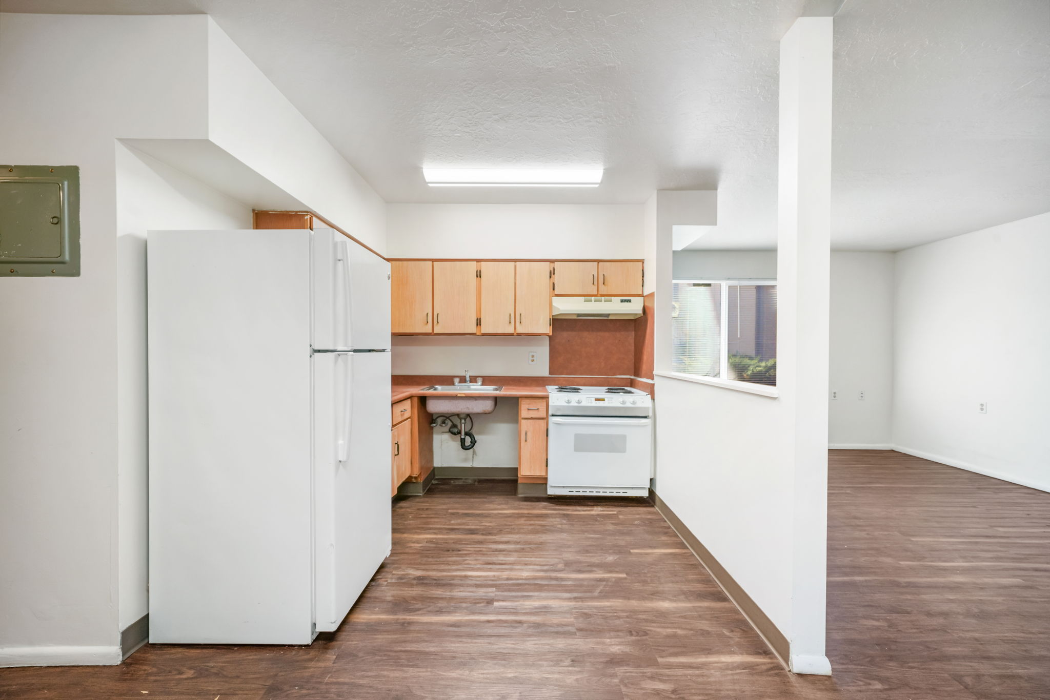 Kitchen with white appliances, dark wood-style floors, light countertops, electric panel, and light wood finish cabinets