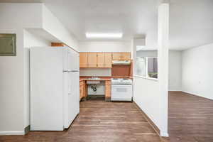 Kitchen with white appliances, dark wood-style floors, light countertops, electric panel, and light wood finish cabinets