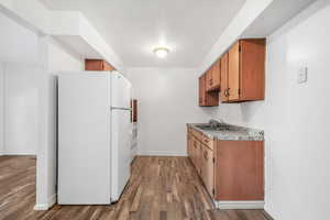 Kitchen with white appliances, wood finish cabinets, light countertops, and dark wood-type flooring