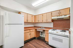 Kitchen featuring white appliances, light wood finish cabinetry, light countertops, and dark wood-style flooring