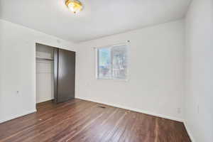 Unfurnished bedroom with a closet and dark wood-style flooring
