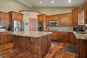 Kitchen featuring vaulted ceiling, stainless steel appliances, light stone countertops,  wood-style flooring, and a center island