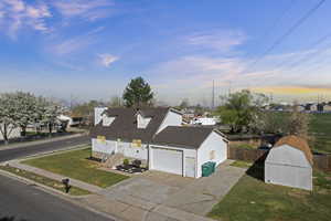 View of front facade featuring driveway, a chimney, a shingled roof, a storage shed, and a residential view