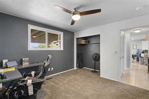 Office space featuring a ceiling fan, light carpet, a textured ceiling, and light tile patterned floors