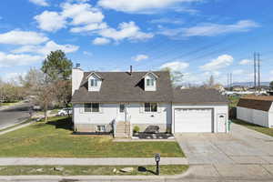 Cape cod-style house with a garage, driveway, a front yard, and a chimney