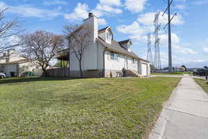 View of side of property featuring a chimney, a yard, and roof with shingles