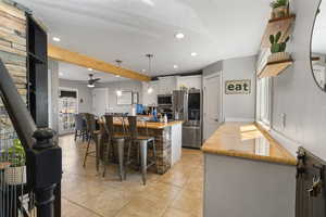 Kitchen featuring stainless steel appliances, beamed ceiling, white cabinetry, a kitchen bar, and an island with sink
