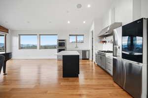 Dual tone kitchen featuring stainless steel appliances, lofted ceiling, a kitchen island, light wood flooring, and quartz countertops
