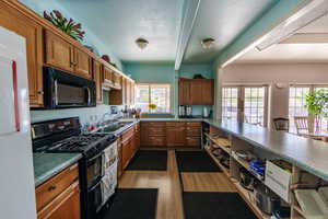 Kitchen with black appliances, wood finish cabinets, french doors, a peninsula, and light wood-style floors