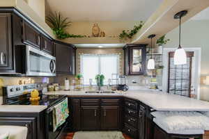 Kitchen with dark wood finish cabinets, electric stove, a peninsula, stainless steel microwave, and pendant lighting