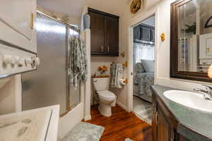 Bathroom with vanity, combined bath / shower with glass door, dark wood-type flooring, washer / clothes dryer, and ensuite bath