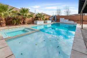 Combined pool / hot tub featuring a patio area, a water slide, and a fenced backyard