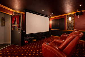 Home theater with ornamental molding, dark carpet, and a textured ceiling