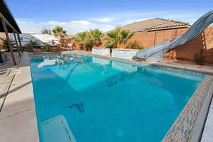 View of pool with a water slide, a fenced backyard, and patio surround