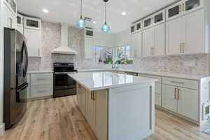 Kitchen featuring glass insert cabinets, refrigerator with ice dispenser, stainless steel electric range oven, a center island, and decorative light fixtures