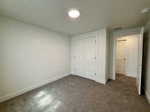 Unfurnished bedroom featuring dark colored carpet, a closet, and a textured ceiling