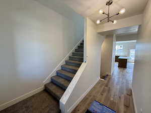 Stairway with wood finished floors and a chandelier