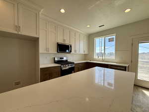 Two tone kitchen with stainless steel appliances, backsplash, recessed lighting, a textured ceiling, and light stone counters