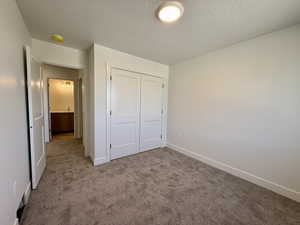 Unfurnished bedroom with dark carpet, a closet, and a textured ceiling