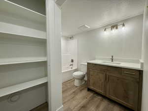 Bathroom with vanity, a textured ceiling, dark wood-type flooring, and shower / washtub combination
