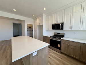 Kitchen with two tone cabinetry, stainless steel appliances, light stone counters, a kitchen island, and light wood-style floors