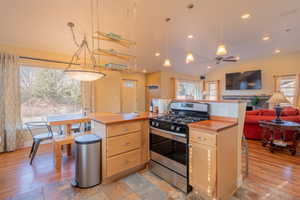 Kitchen featuring stainless steel gas range oven, light wood finish cabinets, open floor plan, a kitchen breakfast bar, and vaulted ceiling