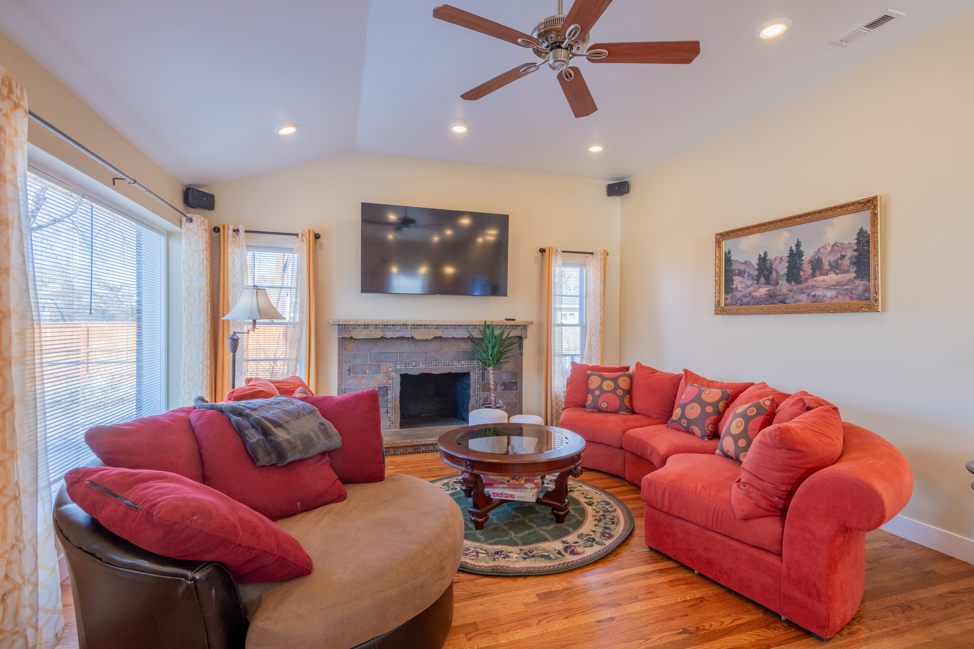 Living room featuring wood finished floors, lofted ceiling, recessed lighting, ceiling fan, and a stone fireplace
